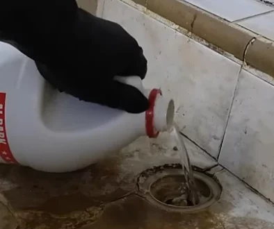 A plumber pouring a specialized acidic solution into a clogged household drain.