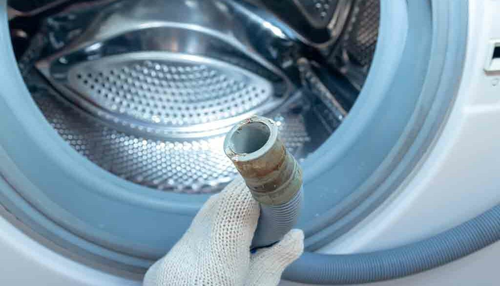 Person holding the drain pipe of a washing machine drum, illustrating how to effectively use a drain unblocker in washing machines.